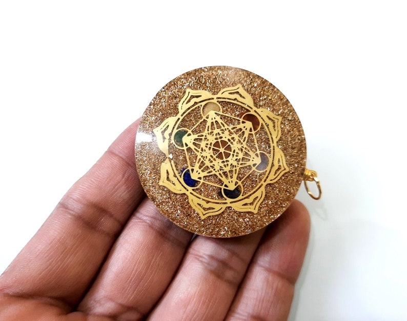 May include: Gold-toned pendant with a clear resin base and a gold-colored geometric design. The design features a flower-like shape with seven points, each containing a different colored gemstone. The pendant has a gold-colored loop for attaching a chain.