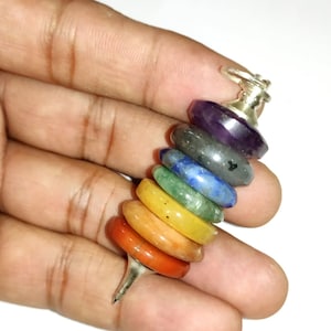 Op de afbeelding: Een zeven-chakra-pendulum met een zilveren ketting en een puntige punt. Het pendulum is gemaakt van zeven gestapelde ringen van verschillende gekleurde edelstenen, die de zeven chakra's voorstellen.