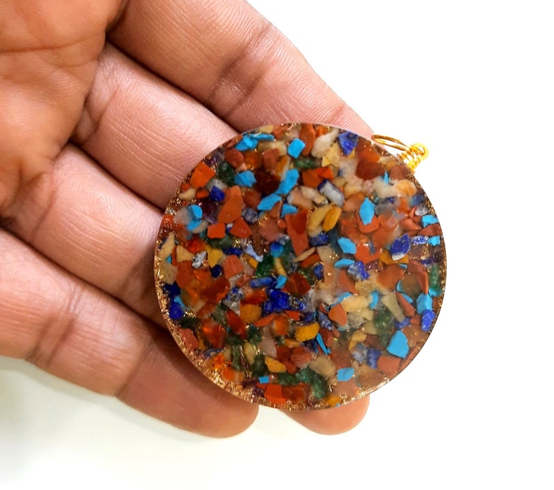 May include: A round, multi-colored, crystal pendant with a gold wire loop. The pendant is made of many small, colorful stones, including red, orange, yellow, green, blue, and purple.