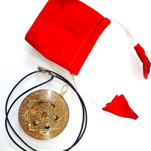May include: A gold-colored pendant with a geometric design and seven colored stones, on a black cord, with a red velvet pouch.