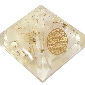 May include: A pyramid-shaped, clear resin object with gold flakes and a gold-colored, oval-shaped design. The design features a geometric pattern. The pyramid is on a white background.