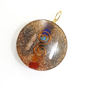 May include: A round, clear pendant with a gold bail. The pendant contains a variety of crystals and a copper wire design in the shape of a double helix. The crystals are embedded in a clear resin.