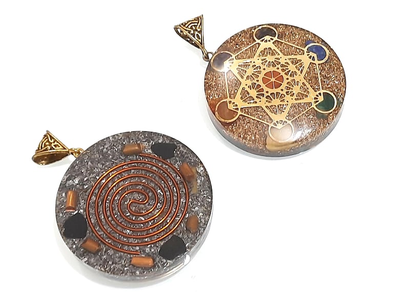 Pu&ograve; includere: Due ciondoli rotondi con anelli di metallo dorati. Il ciondolo a sinistra ha uno sfondo argentato con un design a spirale color rame e pietre nere. Il ciondolo a destra ha uno sfondo marrone con un design geometrico dorato e pietre colorate.