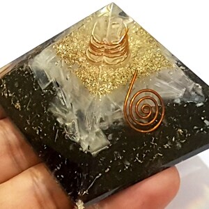 May include: Black obsidian pyramid with a clear quartz crystal and gold glitter on top. A copper wire coil is placed on top of the quartz crystal.