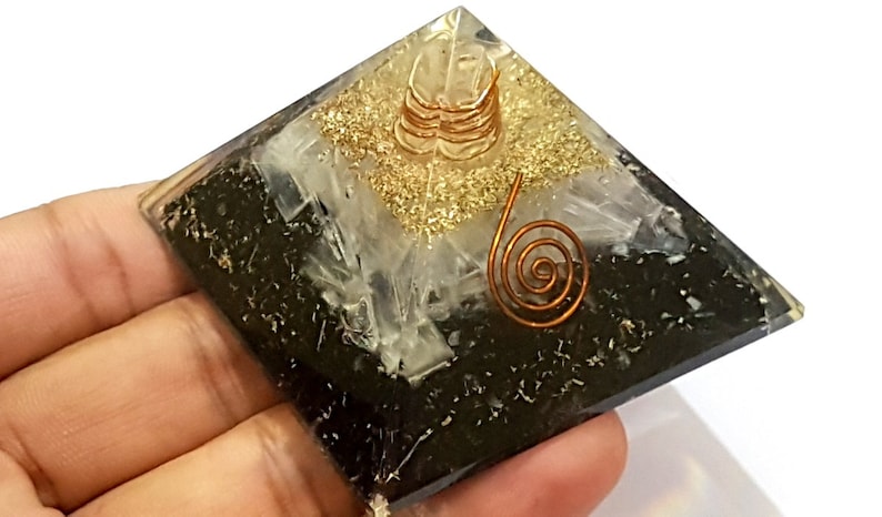 May include: Black obsidian pyramid with a clear quartz crystal and gold glitter on top. A copper wire coil is placed on top of the quartz crystal.