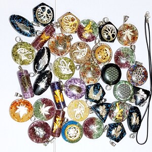 May include: A collection of colorful, crystal pendants with various symbols and designs. The pendants are made of clear resin with embedded crystals and feature symbols like the Eye of Horus, a tree of life, and a flower of life. The pendants are strung on silver chains.