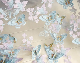 Può includere: Un tessuto bianco trasparente con delicati ricami di farfalle blu e viola. Il tessuto è morbido, arioso e perfetto per l'artigianato o la decorazione.