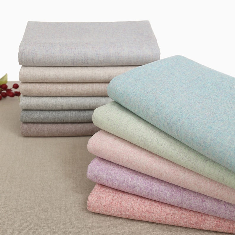 May include: A stack of fabric swatches in various pastel colours, including light blue, green, pink, and purple. The fabric has a subtle texture and a slightly speckled appearance.