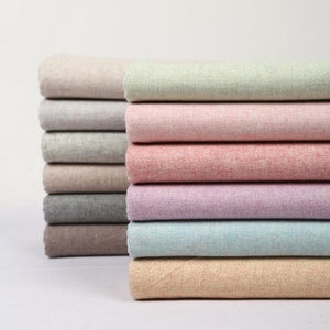 May include: A stack of fabric swatches in various colours, including beige, light green, pink, purple, blue, and peach. The fabric has a textured, slightly fuzzy appearance.