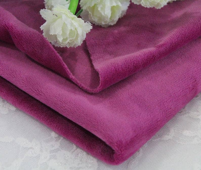 May include: Close-up of a soft, plush fabric in a deep pink hue. The fabric is folded and has a velvety texture.