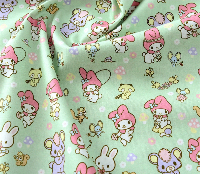 K&ouml;nnte beinhalten: Gr&uuml;ner Stoff mit einem sich wiederholenden Muster aus rosa und wei&szlig;en Comicfiguren, Pilzen und anderen kleinen Details. Die Figuren tragen rosa Schleifen und haben gro&szlig;e Augen.