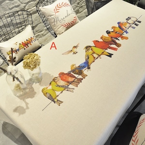 Könnte beinhalten: Eine weiße Tischdecke mit einer Reihe bunter Vögel, die auf einem Draht sitzen. Die Vögel sind realistisch gemalt und umfassen einen Kolibri, einen Kardinal und einen Blauhäher. Die Tischdecke ist mit dem Buchstaben "A" in Rot verziert.