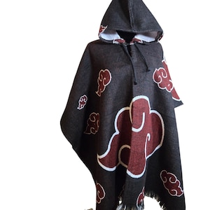 Può includere: Un poncho nero con cappuccio caratterizzato da un motivo ripetuto di nuvole rosse con contorni bianchi. Il capo presenta un cappuccio a punta con cordini neri e un orlo sfrangiato sul fondo, realizzato in un tessuto dalla trama visibile.