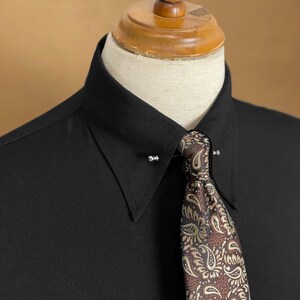 May include: A black dress shirt with a pin collar, paired with a patterned tie. The tie features a brown and gold paisley design. The shirt is displayed on a mannequin.