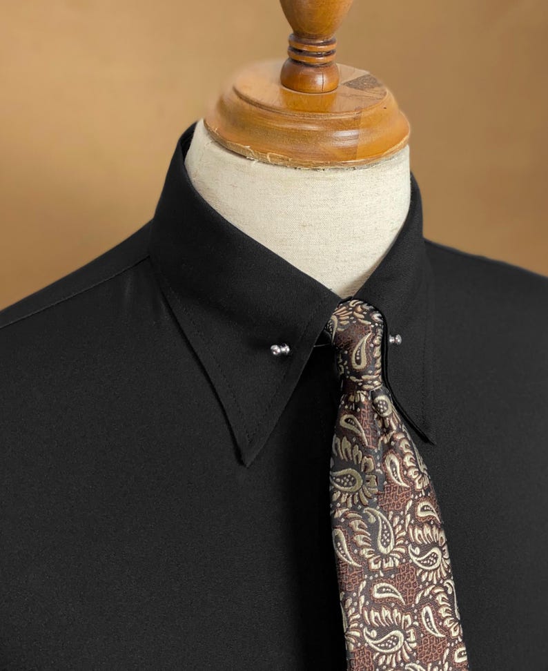 May include: A black dress shirt with a pin collar, paired with a patterned tie. The tie features a brown and gold paisley design. The shirt is displayed on a mannequin.