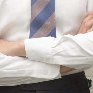May include: White dress shirt with a blue and tan striped tie. The shirt has buttoned cuffs and is paired with dark gray trousers. The image focuses on the upper body, showcasing the classic business attire.