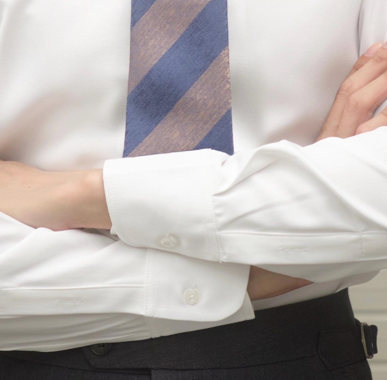 May include: White dress shirt with a blue and tan striped tie. The shirt has buttoned cuffs and is paired with dark gray trousers. The image focuses on the upper body, showcasing the classic business attire.