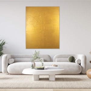 May include: A gold abstract painting with a textured surface hangs on a white wall above a white sofa and a brown leather armchair in a modern living room.