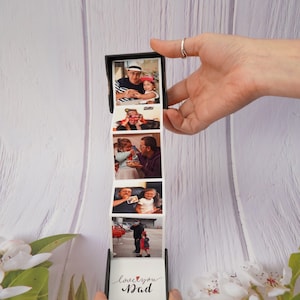 May include: A black photo cube with a white background and a series of photos of a father and daughter. The cube is open and the photos are visible. The last photo in the cube has the text "love you Dad" with a red heart.