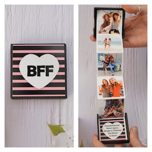 May include: A small black box with pink and black stripes and a white heart with the letters "BFF" in black. The box is open and reveals a series of photos of two friends. The last photo is a heart with the text "Friends Forever Never Apart. Maybe in Distance But Never in Heart."