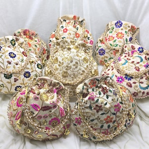 May include: A collection of embroidered drawstring bags in various floral designs. The bags feature cream-colored fabric with colorful floral embroidery, beaded trim, and gold accents. The bags are in different shapes and sizes.