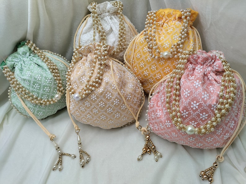 Elegant handmade embroidered potli bag crafted from premium silk fabric featuring intricate floral thread work and golden drawstring closure. Traditional Indian ethnic purse perfect for weddings, bridal gifts, party favors and festive occasions. Soft fabric, spacious design ideal for storing jewelry, cash, makeup and small essentials. Beautiful return gift option for guests.
