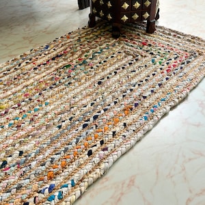 May include: A multi-colored braided rug with a white background. The rug is made of recycled materials and has a natural, rustic look.