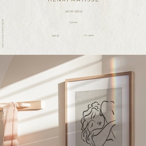 Op de afbeelding: Een ingelijste zwart-witte lijntekening van twee mensen die elkaar omhelzen. De tekening is op een getextureerde beige achtergrond. De lijst is van lichtbruin hout.