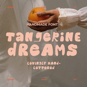 May include: A digital graphic featuring the words "Tangerine Dreams" in a chunky, peach-colored font. The words "Handmade Font" and "Lovingly Hand-Lettered" are also present. An orange is held in a hand, with a neutral background.