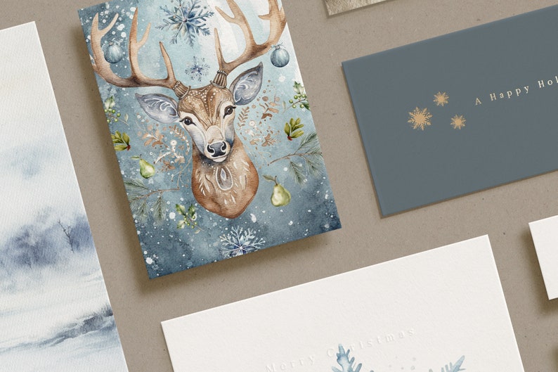 May include: A selection of Christmas greeting cards. One card displays a watercolour illustration of a deer head with antlers, snowflakes, and pear accents. Another card is blue with gold snowflakes and the text "A Happy Hol". A third card has "Merry Christmas" text.