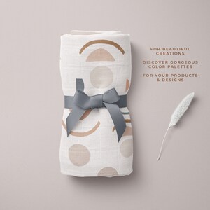 Op de afbeelding: Een witte muslin-wikkeldeken met een geometrisch patroon in tinten bruin, roze en groen. De deken is vastgebonden met een grijs lint en is doormidden gevouwen. De tekst "FOR BEAUTIFUL CREATIONS DISCOVER GORGEOUS COLOR PALETTES FOR YOUR PRODUCTS & DESIGNS" is gedrukt op een witte achtergrond.