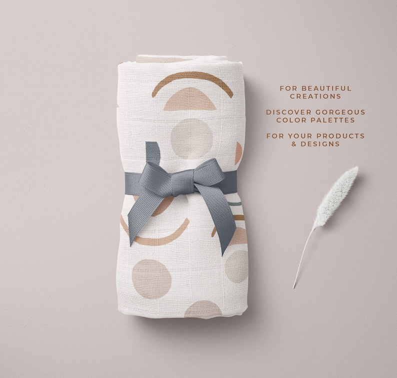 Op de afbeelding: Een witte muslin-wikkeldeken met een geometrisch patroon in tinten bruin, roze en groen. De deken is vastgebonden met een grijs lint en is doormidden gevouwen. De tekst "FOR BEAUTIFUL CREATIONS DISCOVER GORGEOUS COLOR PALETTES FOR YOUR PRODUCTS & DESIGNS" is gedrukt op een witte achtergrond.