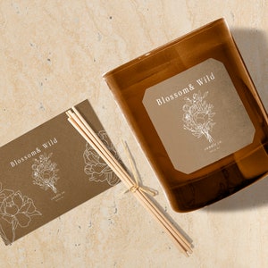 Puede incluir: Un tarro de vela de vidrio marr&oacute;n con una etiqueta que dice "Blossom & Wild candle co.". La etiqueta presenta un dibujo lineal de un ramo de flores. Tambi&eacute;n se muestra un juego de palitos difusores de madera y una tarjeta a juego.