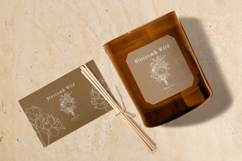 Puede incluir: Un tarro de vela de vidrio marr&oacute;n con una etiqueta que dice "Blossom & Wild candle co.". La etiqueta presenta un dibujo lineal de un ramo de flores. Tambi&eacute;n se muestra un juego de palitos difusores de madera y una tarjeta a juego.