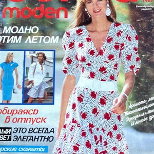 May include: A magazine cover featuring a woman wearing a white and red floral dress with a white belt. The magazine is titled "Burda Moden" and the text "MODNO ЭТИМ ЛЕТОМ" is visible. The magazine cover is from 1987.