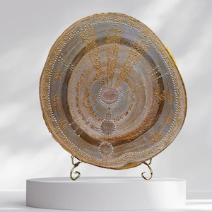 May include: A circular wooden wall hanging with a gold and white design. The design features a central circle with concentric circles around it, and a stylized floral pattern radiating outwards. The piece is mounted on a gold metal stand.