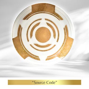 Op de afbeelding: Een witte decoratieve plaat met een gouden geometrisch ontwerp. De plaat heeft concentrische cirkels en hoekige vormen in bladgoud. De tekst "Source Code" staat eronder.