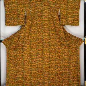 May include: A full-length, patterned kimono in shades of gold, orange, and green. The fabric is covered in a floral design. The garment is displayed on a black frame. The text "Kimono Dream Shop" is visible at the bottom right.