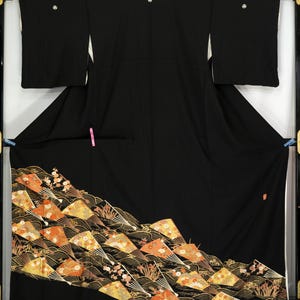 May include: A black kimono with a decorative pattern of fans in shades of orange, yellow, and gold. The fans are set against a black background with gold wave-like lines. The kimono has long sleeves and is displayed in a frame.