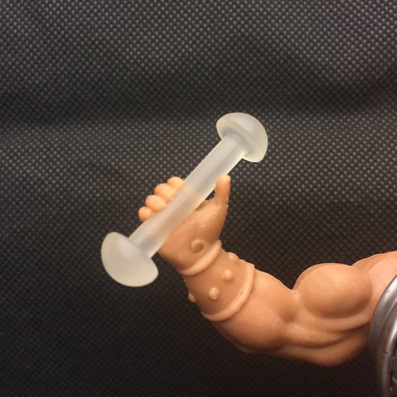 May include: A clear plastic dumbbell with rounded ends. The dumbbell is being held by a muscular arm.
