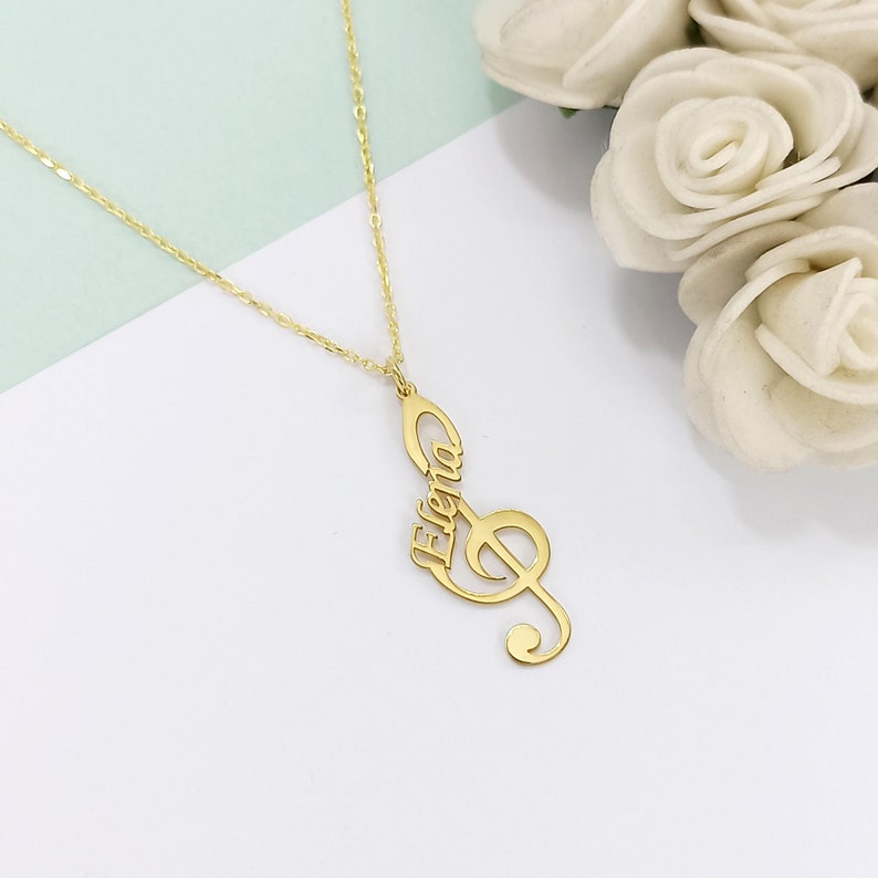 May include: Gold necklace with a treble clef pendant that has the name "Elena" incorporated into the design.