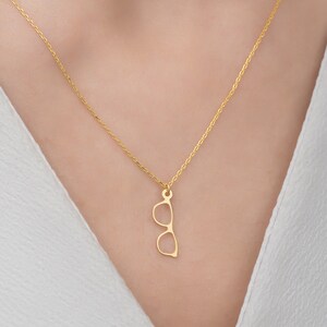 May include: A gold chain necklace with a pendant shaped like a pair of sunglasses.