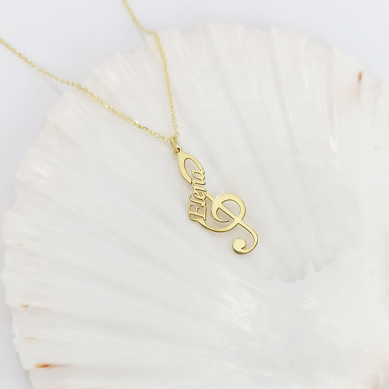 May include: Gold necklace with a treble clef pendant that has the name "Elena" inscribed on it.
