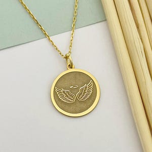 以下が含まれることがあります： 天使の羽根とハローが刻まれた丸いペンダントが付いたゴールドチェーンネックレス。