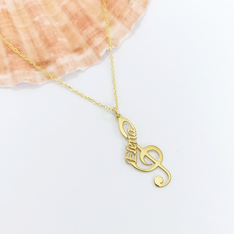 May include: Gold necklace with a treble clef pendant that has the name "Elena" inscribed on it.