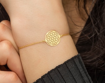 May include: A gold chain bracelet with a round, openwork charm featuring a flower of life design.