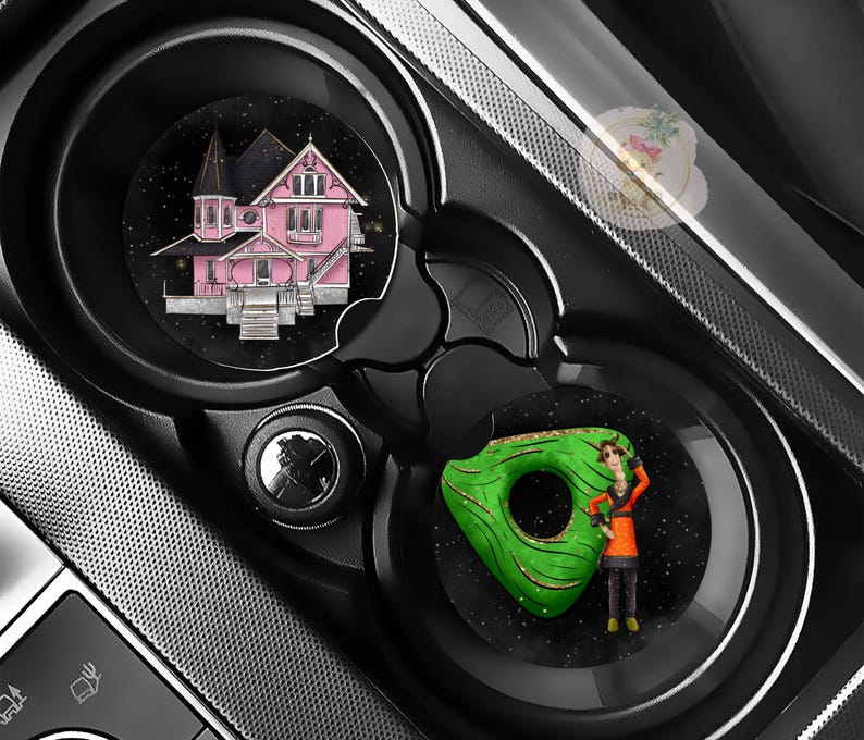 Pu&ograve; includere: Portabicchieri per auto neri con due sottobicchieri circolari. Uno presenta un'illustrazione di una casa rosa, l'altro una ciambella verde con una persona. I sottobicchieri sono su uno sfondo nero con effetto stellato.