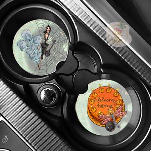 Pu&ograve; includere: Due sottobicchieri per auto con design unici. Uno presenta una donna in abito nero su una ragnatela con fantasmi. L'altro ha una torta arancione con candele accese e una libellula, con la scritta "welcome home!"