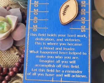 Puede incluir: Un recuerdo azul de madera con temática de fútbol con el texto "Class of 2026" y un gráfico de fútbol. El recuerdo incluye el nombre "Evan" y "SkyView High School". Tiene una cuerda para colgar.