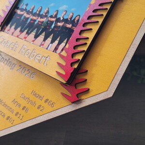 May include: A wooden photo frame with a team photo. The frame is yellow with red accents and the text "Red Wolves 10U", "Coach Robert", and "Spring 2026". Names and numbers are also engraved on the frame.